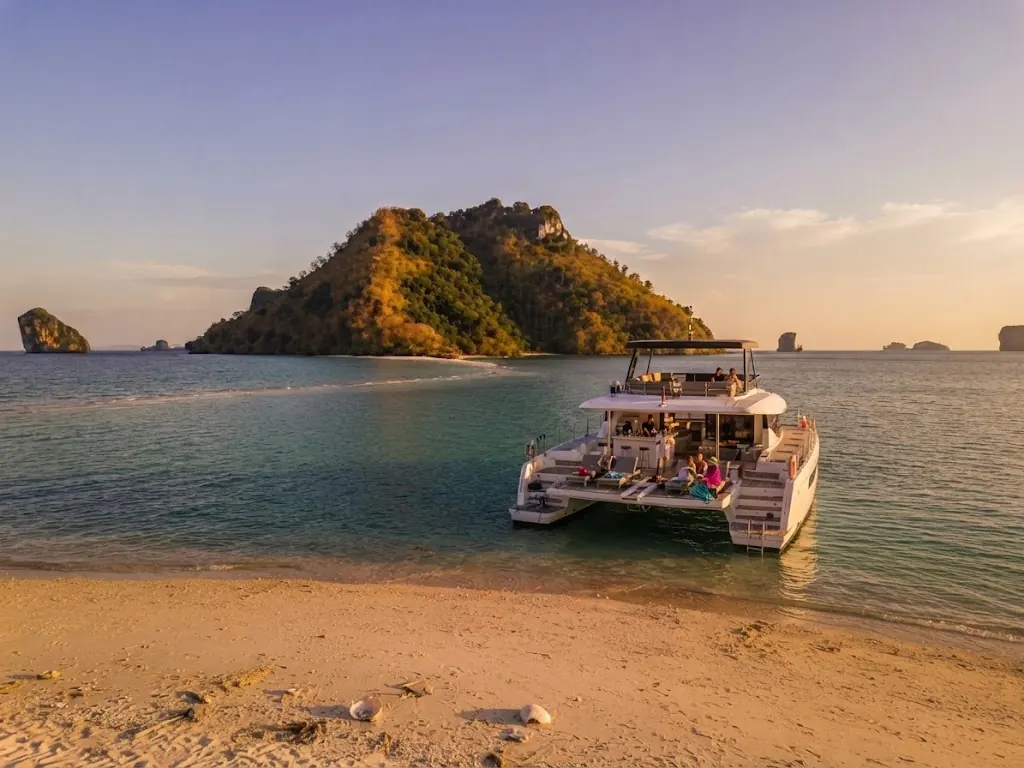 Private catamaran anchored off a sandy beach beside a forested island in Krabi at golden hour