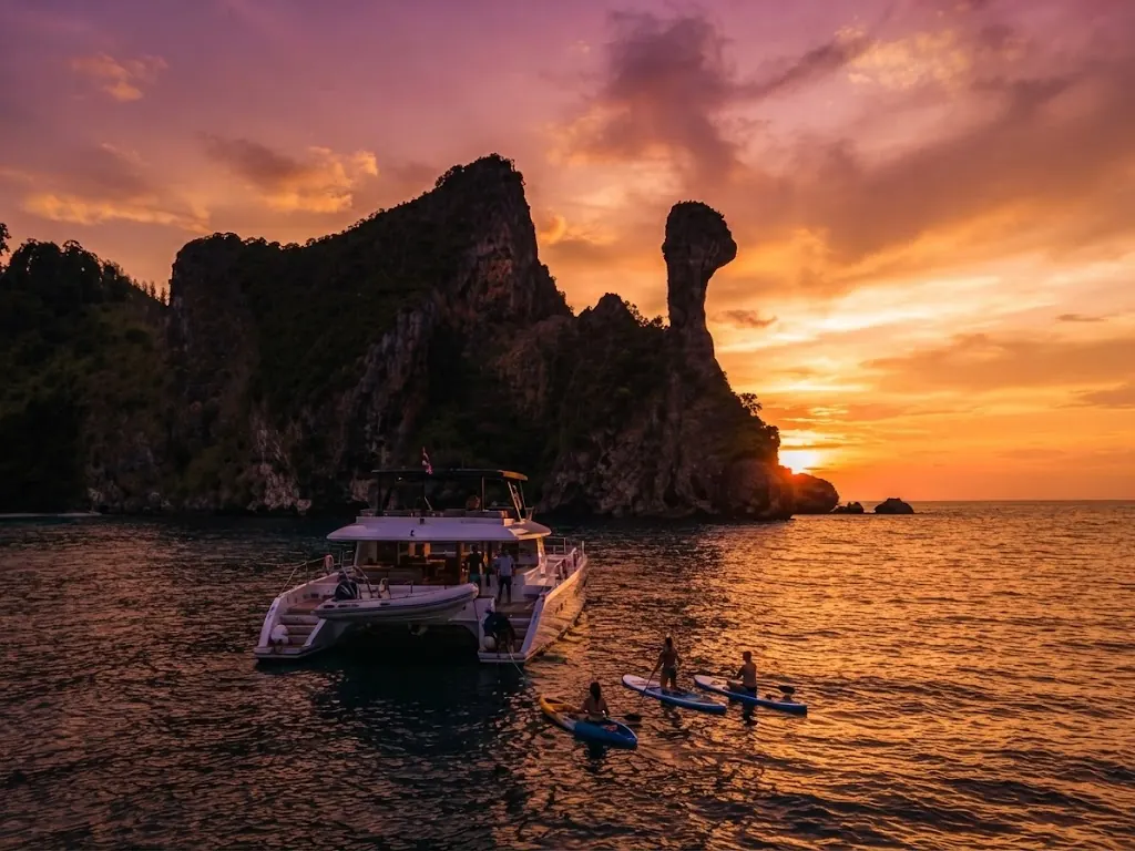 Catamaran and paddleboarders in front of Chicken Island's silhouette at sunset