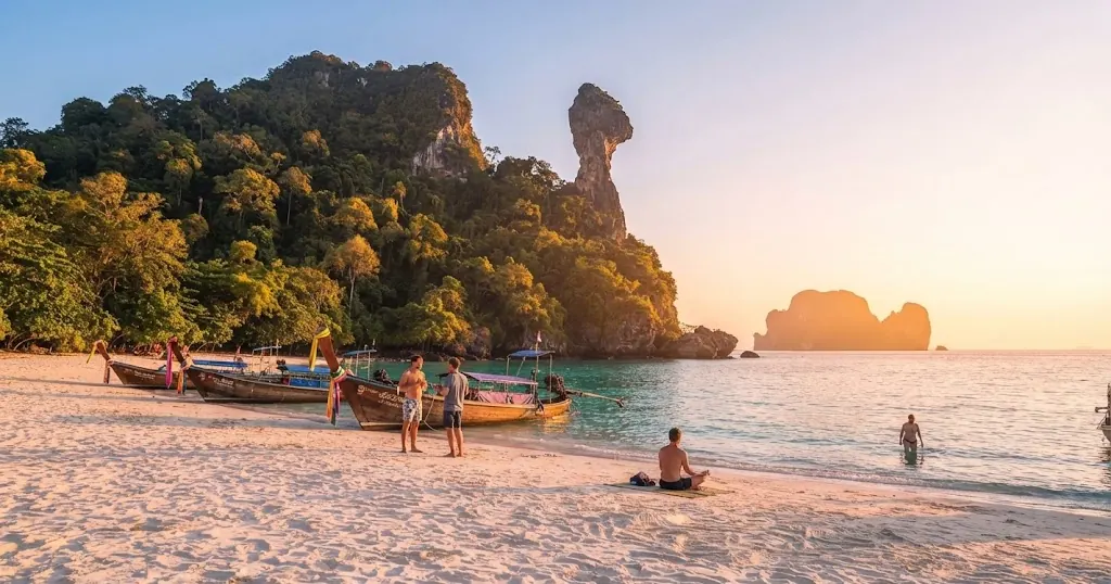 Longtail boats and swimmers on the beach at Chicken Island with the rock formation above