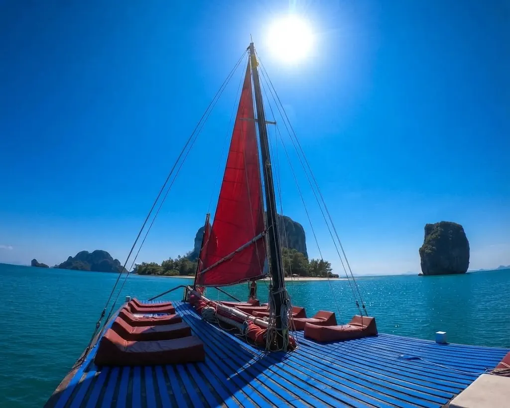 Blue deck and red sail of a cruise boat with limestone islands under a bright sun