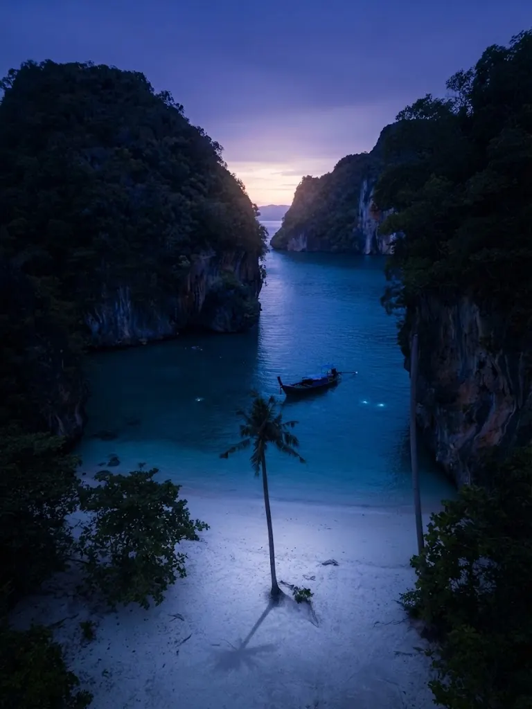 Narrow lagoon between cliffs with a single palm and a boat at blue hour