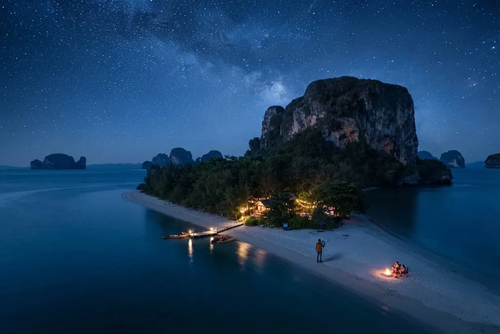 Milky Way over an island beach with a campfire and warm lights at night