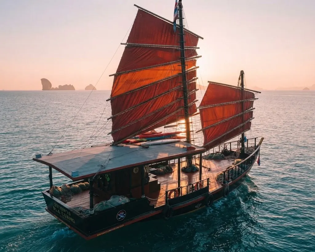 Aerial view of a red-sailed junk boat at sea on a sunset cruise