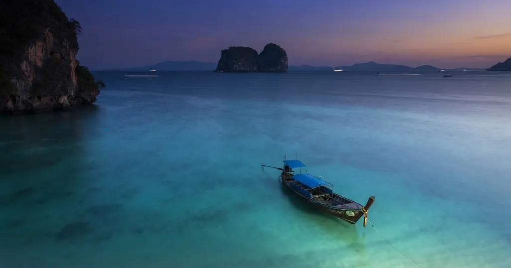 Traditional longtail boat floating in clear turquoise water off Krabi with limestone islets on the horizon