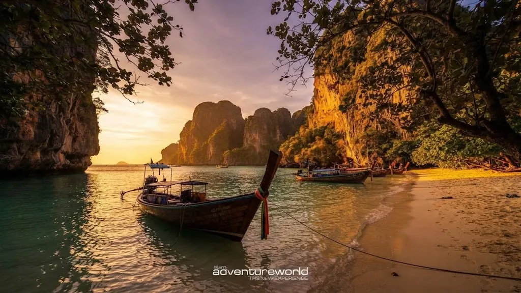 Longtail boat moored in a quiet bay framed by trees and limestone cliffs at sunset