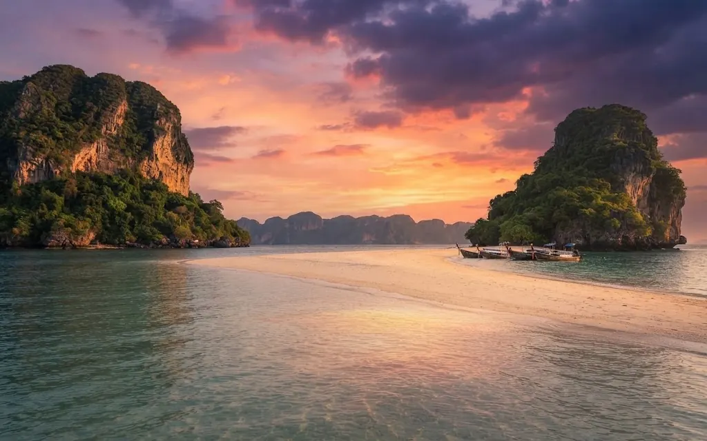 Longtail boats beached between two limestone islands at a pink sunset in Krabi