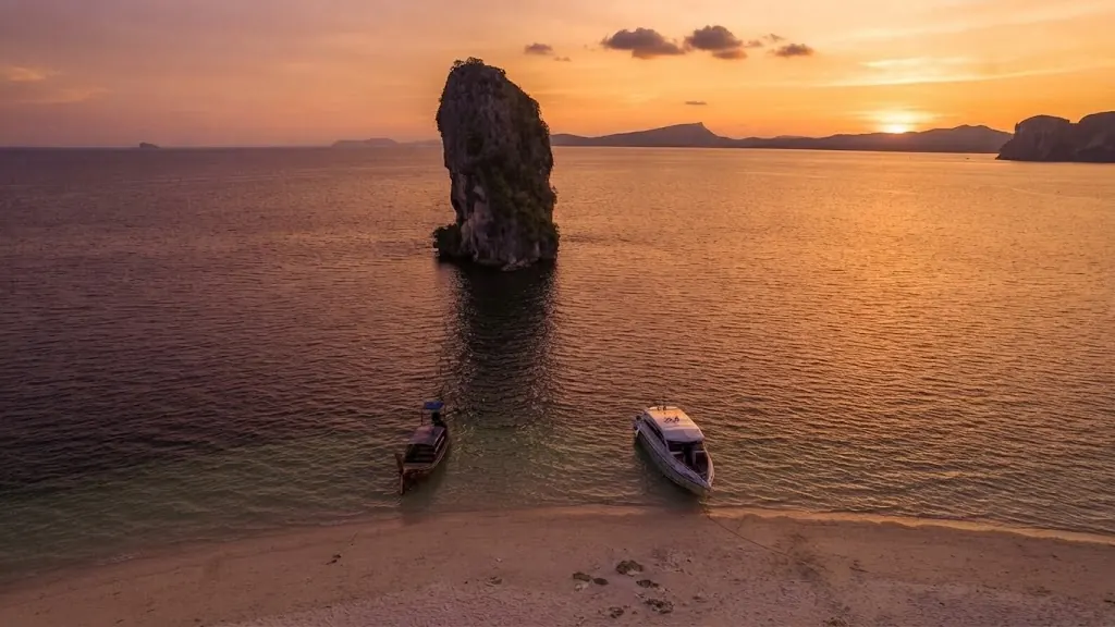 The Poda Island sea stack at sunset with a longtail boat and a speedboat moored off the beach