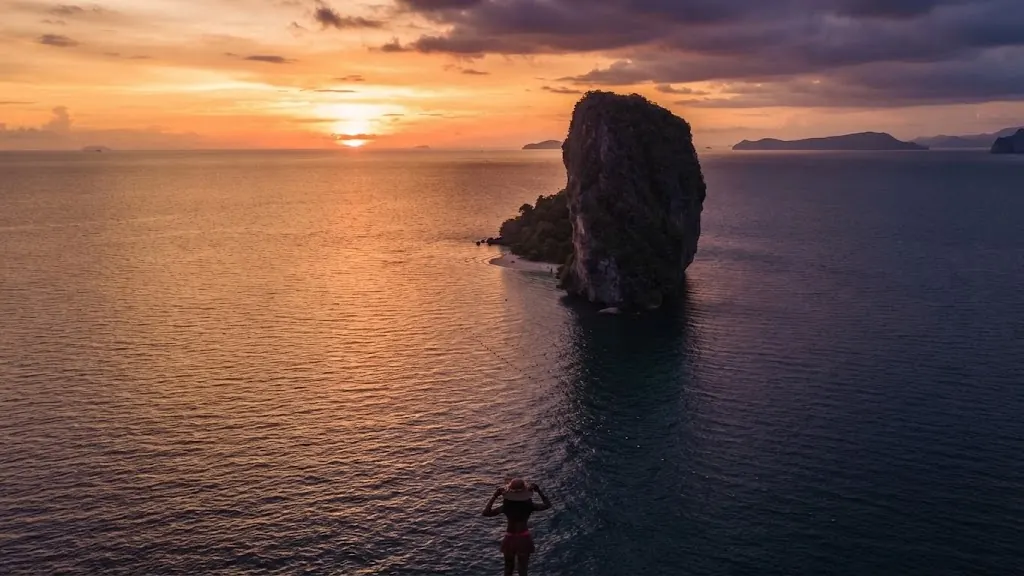 Swimmer in calm water facing the Poda Island sea stack at sunset
