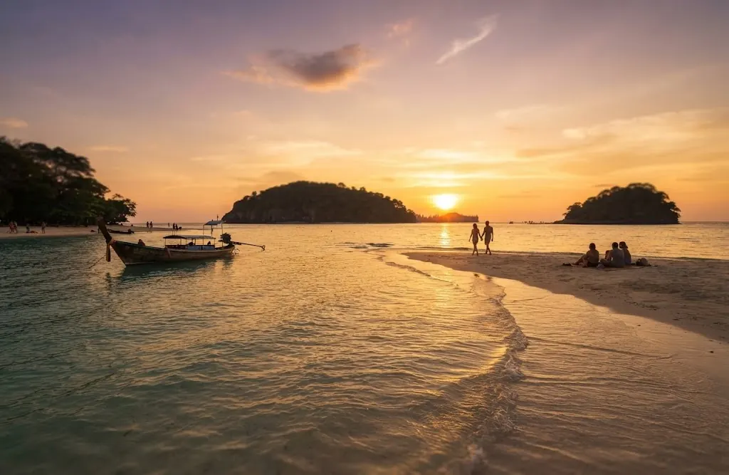 Couple standing on a sandbar between two small islands at sunset with a longtail boat moored
