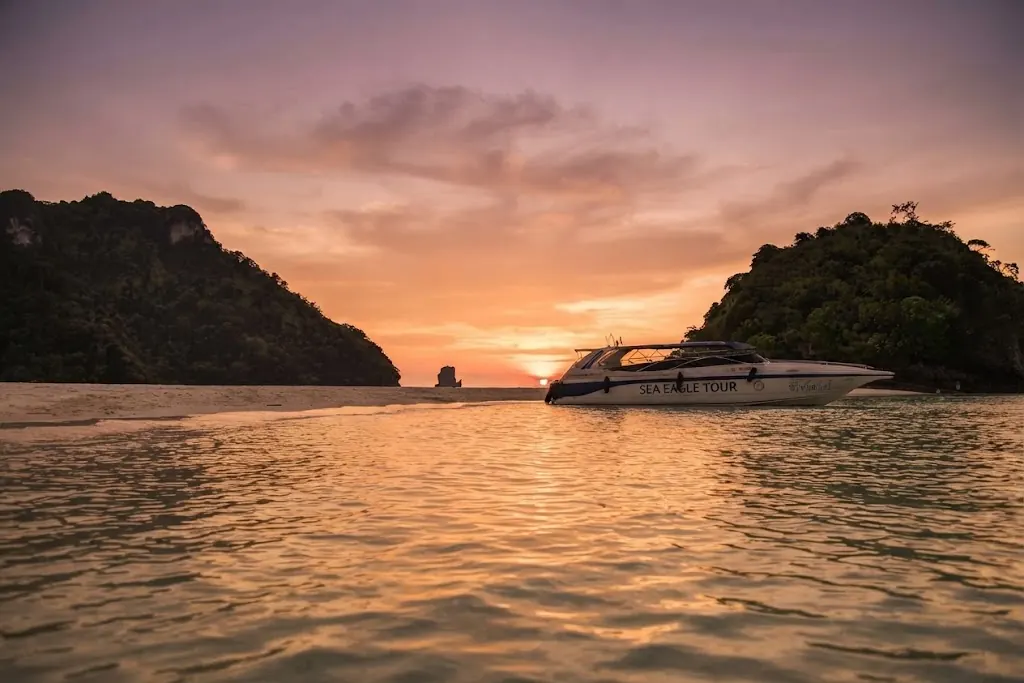 Speedboat anchored in calm water between two islands at sunset