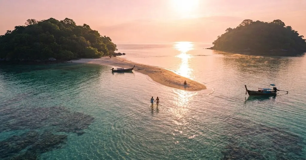 Couple walking the Talay Waek sandbar between Tup and Mor islands at sunset with longtail boats nearby
